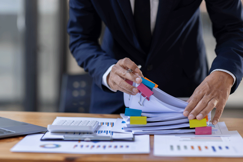 Man thumbing through printed annual reports on desk